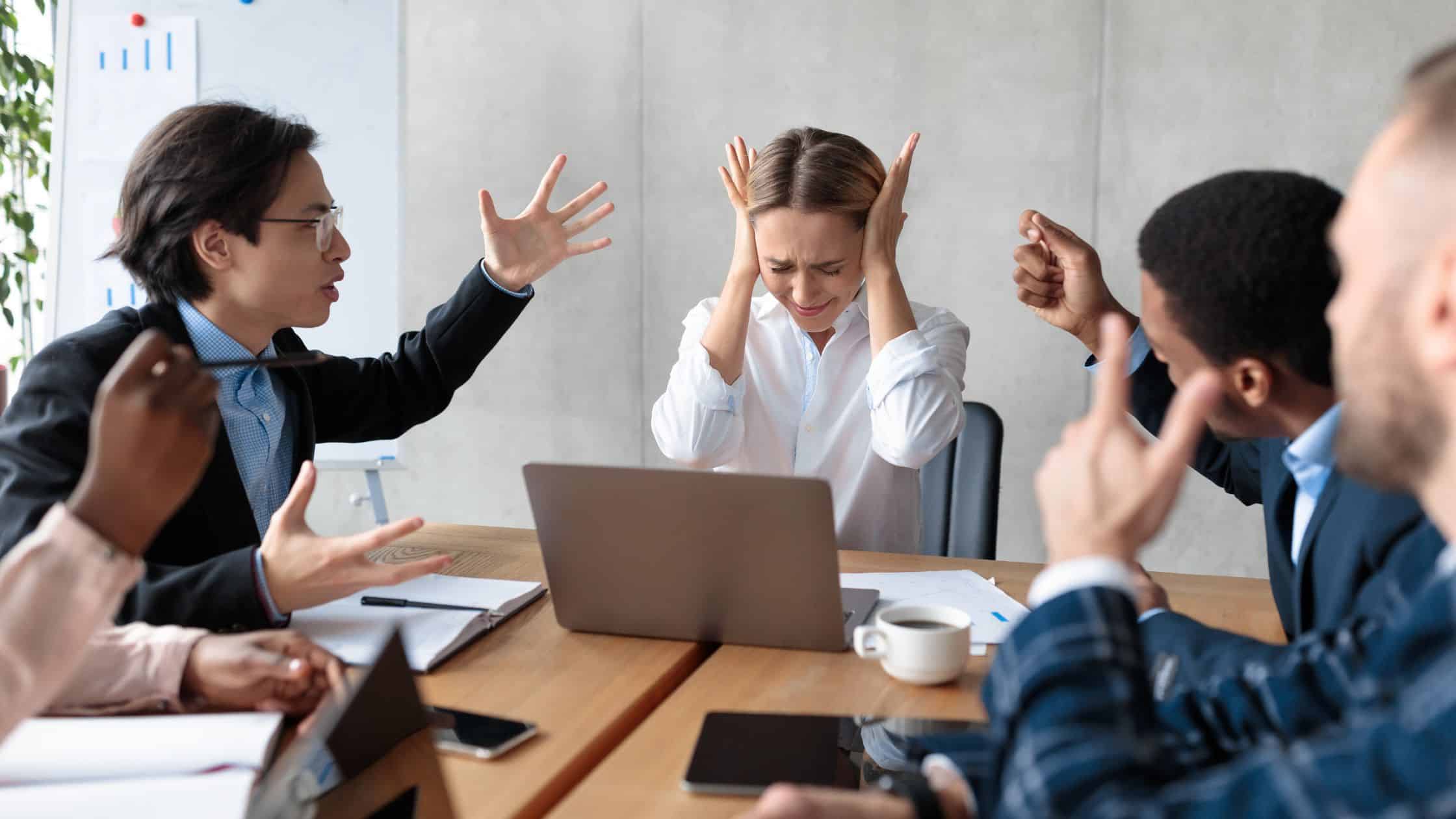 Employees sitting at a table having a discussion, one listening attentively while the other speaks with their arms crossed, demonstrating effective communication and conflict resolution in the workplace.